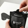 A person's hands are shown holding a black silk mouth tape strip in its black resealable pouch packaging labeled 'TITAN RECOVERY' and 'GOODNIGHT!'.